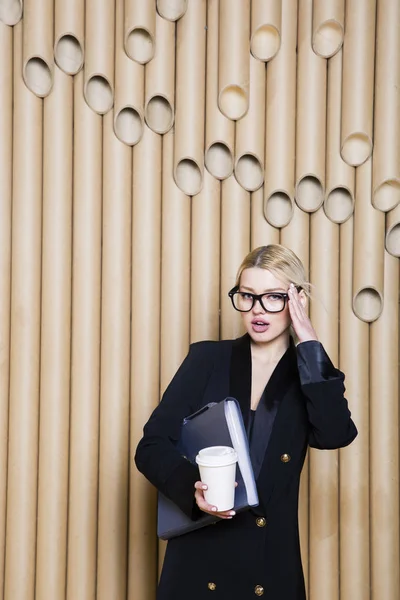 Beautiful amazed blonde business woman in black dress and glasses with coffee mug.