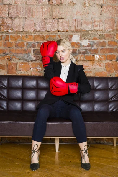 Attractive blond businesswoman with boxing gloves ready for a fight in front of an apartment. Business concept.