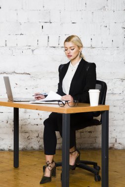 Genç sarışın güzel işkadını dizüstü bilgisayar, dizüstü bilgisayar ve gözlük kıyafetli bir office masada oturuyor. İş kavramı.