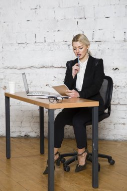 Genç sarışın güzel işkadını dizüstü bilgisayar, dizüstü bilgisayar ve gözlük kıyafetli bir office masada oturuyor. İş kavramı.