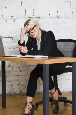 Genç sarışın güzel işkadını dizüstü bilgisayar, dizüstü bilgisayar ve gözlük kıyafetli bir office masada oturuyor. İş kavramı.