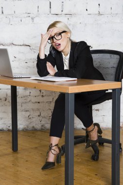 Genç sarışın güzel işkadını dizüstü bilgisayar, dizüstü bilgisayar ve gözlük kıyafetli bir office masada oturuyor. İş kavramı.