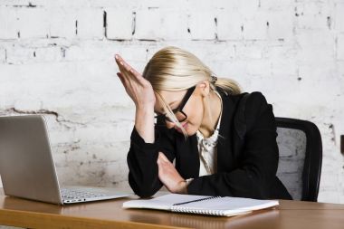 Genç sarışın güzel işkadını dizüstü bilgisayar, dizüstü bilgisayar ve gözlük kıyafetli bir office masada oturuyor. İş kavramı.