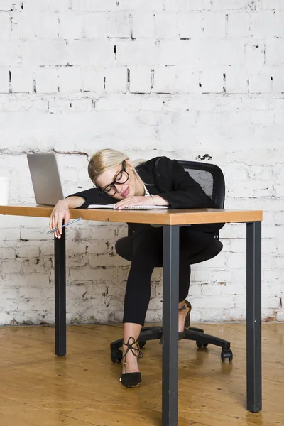 Genç sarışın güzel işkadını dizüstü bilgisayar, dizüstü bilgisayar ve gözlük kıyafetli bir office masada oturuyor. İş kavramı.