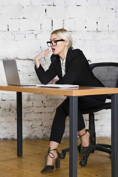 Young blond beauty businesswoman sitting at a office table with laptop, notebook and glasses in suit. Business concept. — Stock Photo, Image