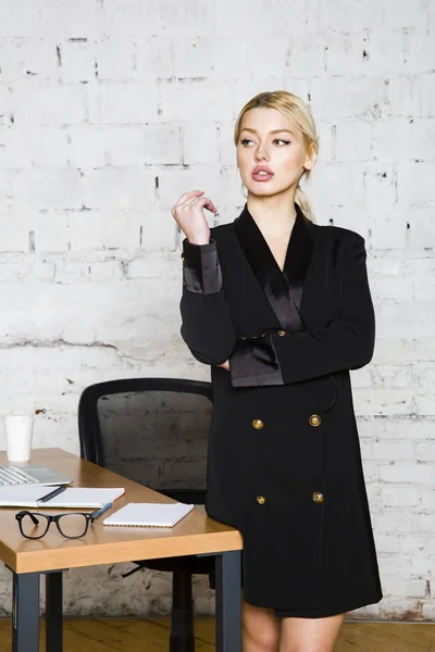 Joven mujer de negocios rubia de belleza sentada en una mesa de oficina con portátil, portátil y gafas de traje. Concepto empresarial . — Foto de Stock