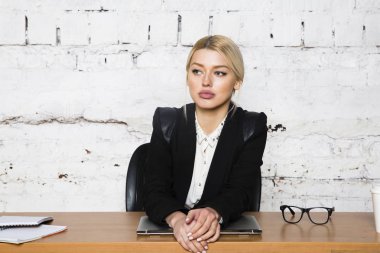 Genç sarışın güzel işkadını dizüstü bilgisayar, dizüstü bilgisayar ve gözlük kıyafetli bir office masada oturuyor. İş kavramı.