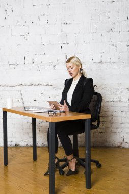 Genç sarışın güzel işkadını dizüstü bilgisayar, dizüstü bilgisayar ve gözlük kıyafetli bir office masada oturuyor. İş kavramı.