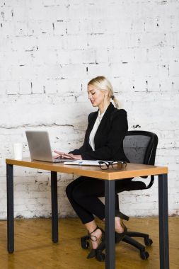 Genç sarışın güzel işkadını dizüstü bilgisayar, dizüstü bilgisayar ve gözlük kıyafetli bir office masada oturuyor. İş kavramı.