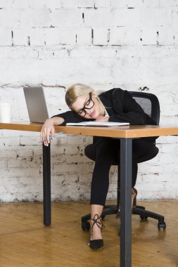 Genç sarışın güzel işkadını dizüstü bilgisayar, dizüstü bilgisayar ve gözlük kıyafetli bir office masada oturuyor. İş kavramı.