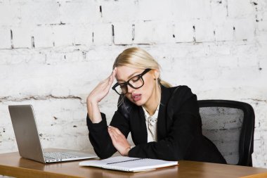 Genç sarışın güzel işkadını dizüstü bilgisayar, dizüstü bilgisayar ve gözlük kıyafetli bir office masada oturuyor. İş kavramı.