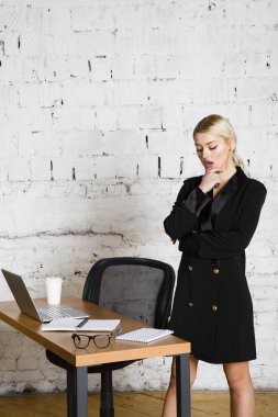 Genç sarışın güzel işkadını dizüstü bilgisayar, dizüstü bilgisayar ve gözlük kıyafetli bir office masada oturuyor. İş kavramı.