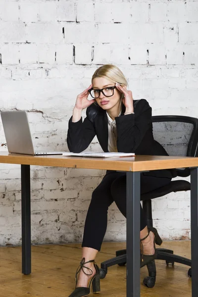 Young blond beauty businesswoman sitting at a office table with laptop, notebook and glasses in suit. Business concept. — Stock Photo, Image
