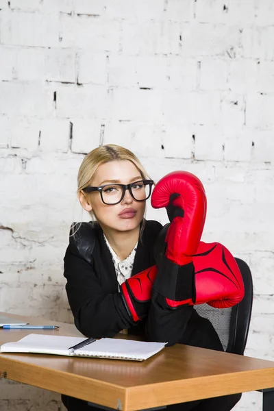 Joven mujer de negocios rubia de belleza sentada en una mesa de oficina con portátil, portátil y gafas en traje y guantes de boxeo . — Foto de Stock