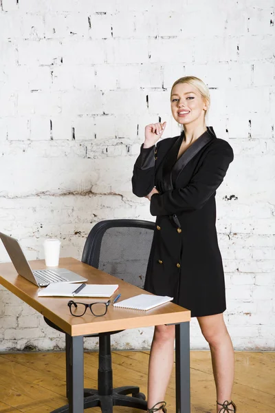年轻的金发美女女实业家坐在办公室的桌子上, 笔记本电脑, 笔记本和眼镜的西装。经营理念. — 图库照片