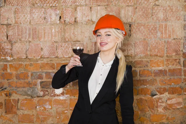 Mimar öğrenci veya ressam kadeh şarap ile portresi ve miğfer korumak. Tuğla kırmızı arka plan.