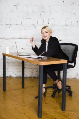 Genç sarışın güzel işkadını dizüstü bilgisayar, dizüstü bilgisayar ve gözlük kıyafetli bir office masada oturuyor. İş kavramı.