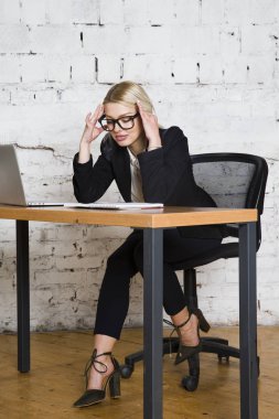 Genç sarışın güzel işkadını dizüstü bilgisayar, dizüstü bilgisayar ve gözlük kıyafetli bir office masada oturuyor. İş kavramı.