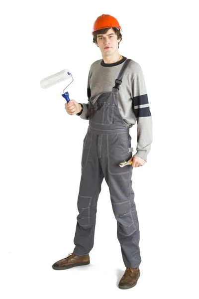 A young man in working grey clothes and orange hard helmet painting the walls in the room. — Stock Photo, Image