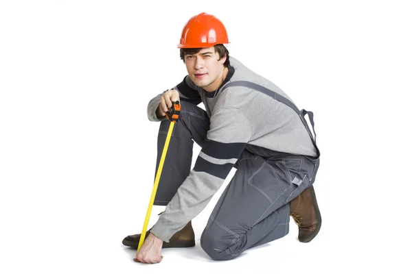 Um jovem em roupas cinza de trabalho e capacete laranja duro medindo a área métrica na sala . — Fotografia de Stock