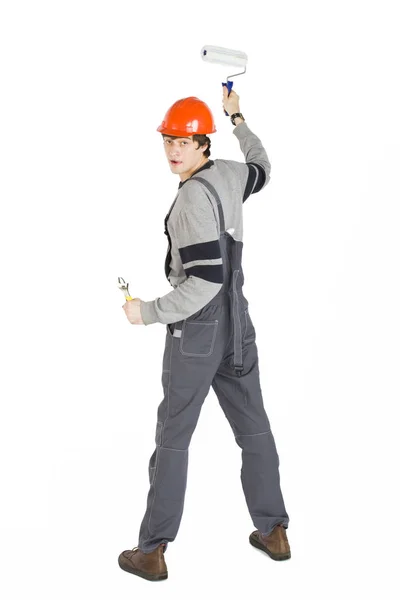 Un giovane uomo in abiti grigi di lavoro e casco duro arancione dipingere le pareti della stanza . — Foto Stock