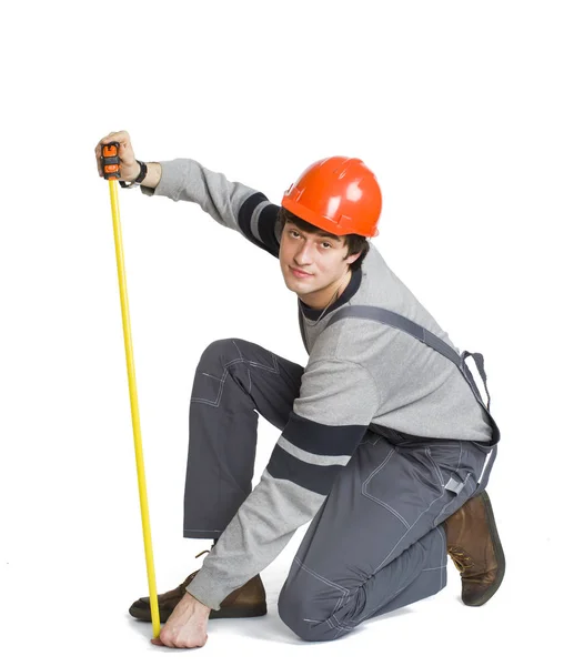 Молодой человек в серой одежде и оранжевом шлеме измеряет метрическую область в комнате . — стоковое фото