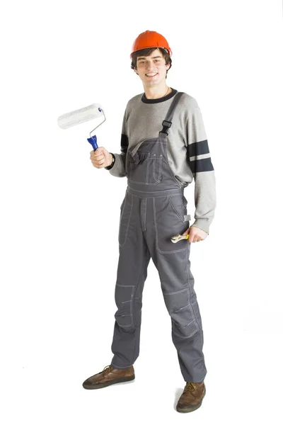 A young man in working grey clothes and orange hard helmet painting the walls in the room. — Stock Photo, Image