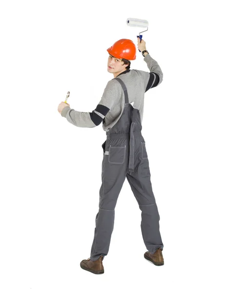 Um jovem em roupas cinza trabalhando e laranja capacete duro pintando as paredes na sala . — Fotografia de Stock