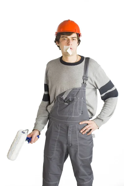 Un joven con ropa gris de trabajo y casco duro naranja con cinta adhesiva sobre la boca. Aislado sobre fondo blanco . — Foto de Stock