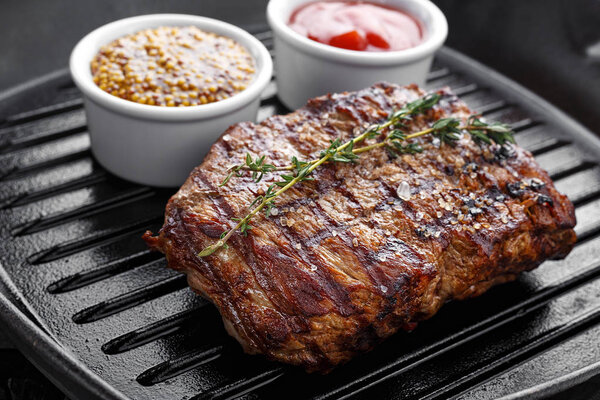 Cooked steak on the grill pan on the steak is herb thyme, there are a number sauces - ketchup and mustard French