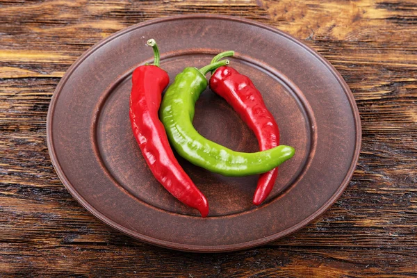 Red and green pepper in a clay plate on dark wooden surface — Stock Photo, Image