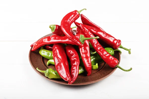 Beyaz ahşap yüzeyde bir kil tabak içinde kırmızı ve yeşil biber