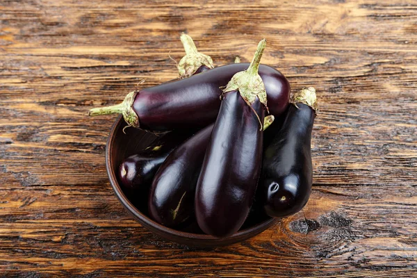 Récolte d'aubergines dans une assiette d'argile sur une vieille table en bois sombre. t — Photo