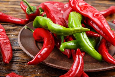 koyu ahşap yüzeyde bir kil tabak içinde kırmızı ve yeşil biber