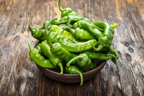 Green chili peppers placed in a clay plate on a brown wooden tab — Stock Photo, Image