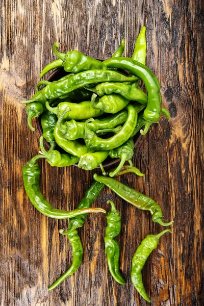 Green chili peppers placed in a clay plate on a brown wooden tab — Stock Photo, Image