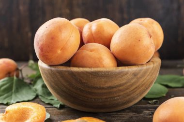 ahşap backgrou üzerinde ahşap bir tabak içinde yapraklarla olgun kayısı