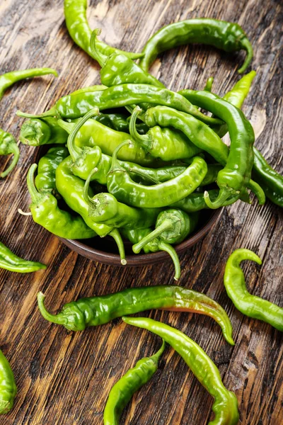 Green chili peppers placed in a clay plate on a brown wooden tab — Stock Photo, Image