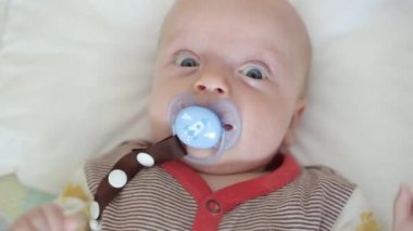 Yeni doğan çocuk bir beşik içinde yatıyor ve düzenli olarak kameraya benziyor