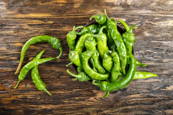 Green chili peppers placed in a clay plate on a brown wooden tab — Stock Photo, Image