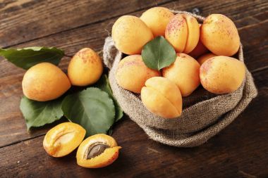 Masanın üzerindeki ahşap kasede lezzetli olgun kayısılar.