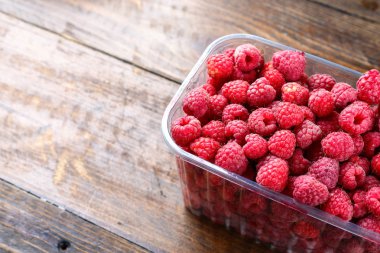 ahşap arka plan üzerinde plastik bir kapta taze frambuaz