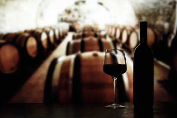 Una copa y una botella de vino sobre el fondo de las barricas — Foto de Stock