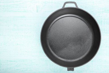 Fresh black cast-iron skillet on a wooden background. 