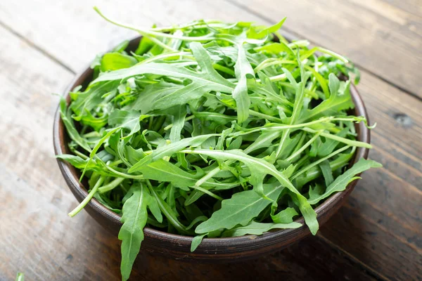Fresh arugula leaves in a bowl on a wooden table. — Stock Photo, Image