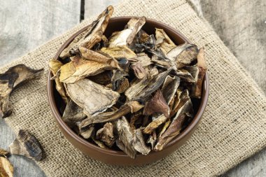 Kurutulmuş mantarlar eski ahşap bir arka planda, bir tabakta dilimlenmiş..