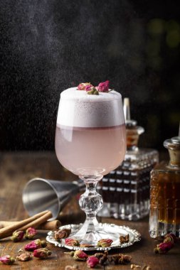 Bardakta köpük olan pembe kadın kokteyli. Kurumuş gülle süslenmiş. Arka planda görünen barmen mucit var.