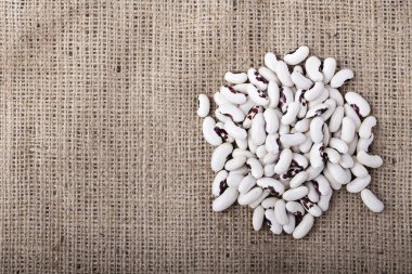 Çuval bezinin arka planına çiğ siyah fasulye serpilmiş. metin için yer.