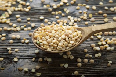 Kahverengi ahşap bir arka planda kaşıkta kuru bezelyeler. Besleyici çorba için fasulye.