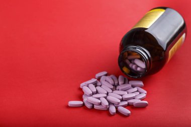 Kırmızı arka plandaki cam kavanozdan yayılmış pembe haplar. tex için yer